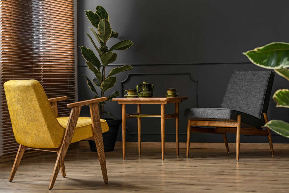 Elegant och mörk lägenhetsinredning med klassiska trämöbler och en stor krukväxt bredvid persienner och en svart vägg med gjutning